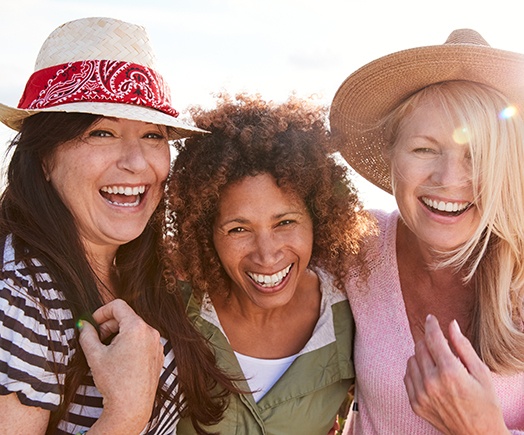 Three smiling middle-aged women standing outdoors