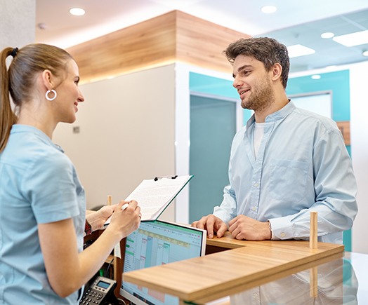 a patient speaking with a front desk staff member of a dental office