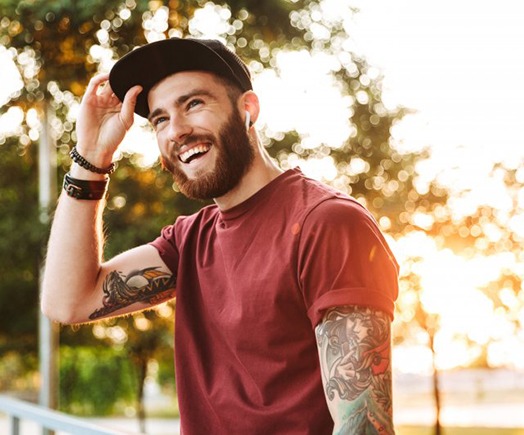 Man smiling while adjusting his hat outdoors